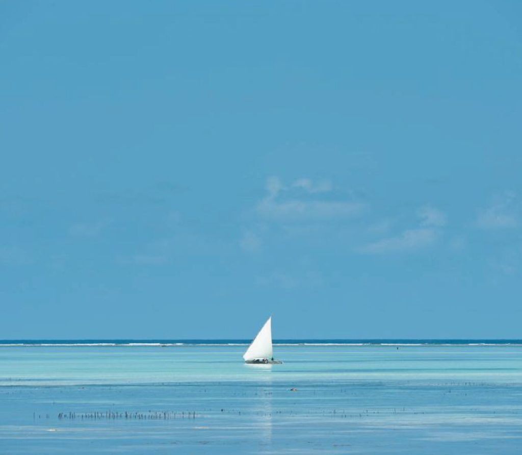 Ruhige Küstenlandschaft bei Be Zanzibar mit weißem Segelboot auf türkisblauem Wasser unter klarem Himmel