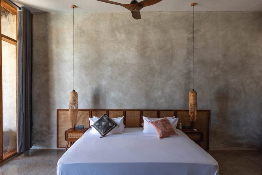 Modernes Beachfront Deluxe Zimmer im Be Zanzibar mit großem Bett, Rattan-Kopfteil und hängenden Lampen aus geflochtenem Stoff