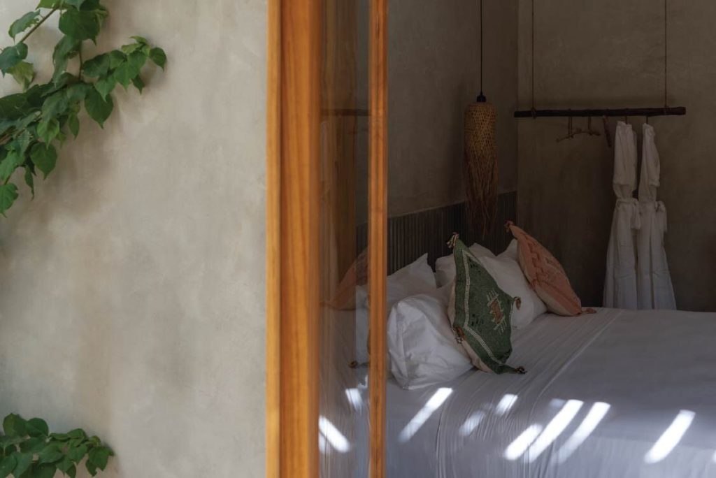 Blick in Be Zanzibar Hawaiian Deluxe Zimmer mit Bett, weißen Laken, grünen Kissen und Holztür