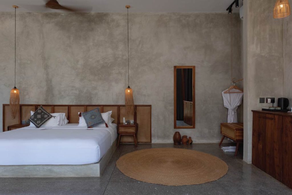Modernes Zimmer der Be Zanzibar King Suite Ocean mit grauer Betonwand, großem Bett und geflochtenen Lichtern