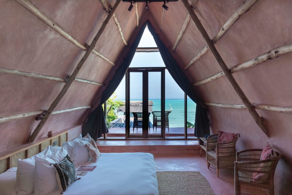 Hotelzimmer Be Zanzibar Ocean Twisted Palm mit spitz zulaufendem Holzdach, großem Bett, geflochtenen Sesseln und Meerblick