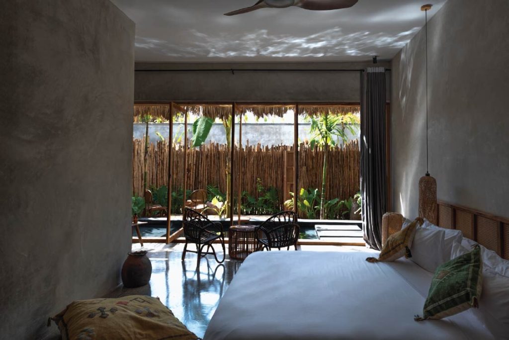 Großes Hotelzimmer mit Bett, Sitzbereich, Glasfront und Terrasse mit Pool und tropischen Pflanzen in Sansibar