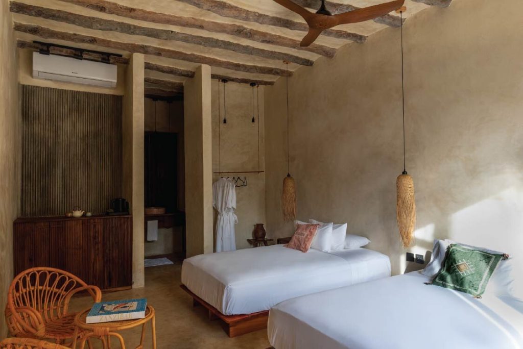 Zimmer Stone Town Twin mit zwei Einzelbetten, Holzbalken, geflochtenen Pendelleuchten und Korbstuhl in Be Zanzibar