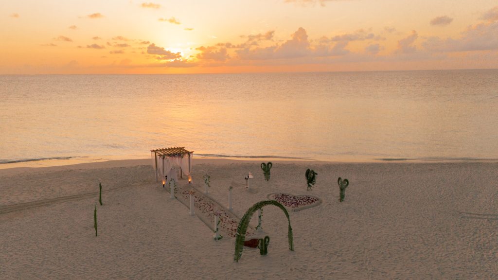Holzpavillon mit Blumen am Strand bei Sonnenuntergang mit Sandweg und Meer im Hintergrund