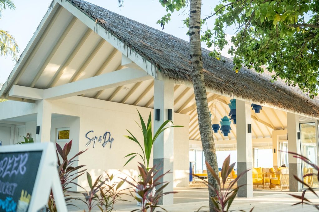 Moderner Barbereich Sip Dip im Eri Maldives mit weißen Wänden, blau-gelben Möbeln und tropischem Strohdach