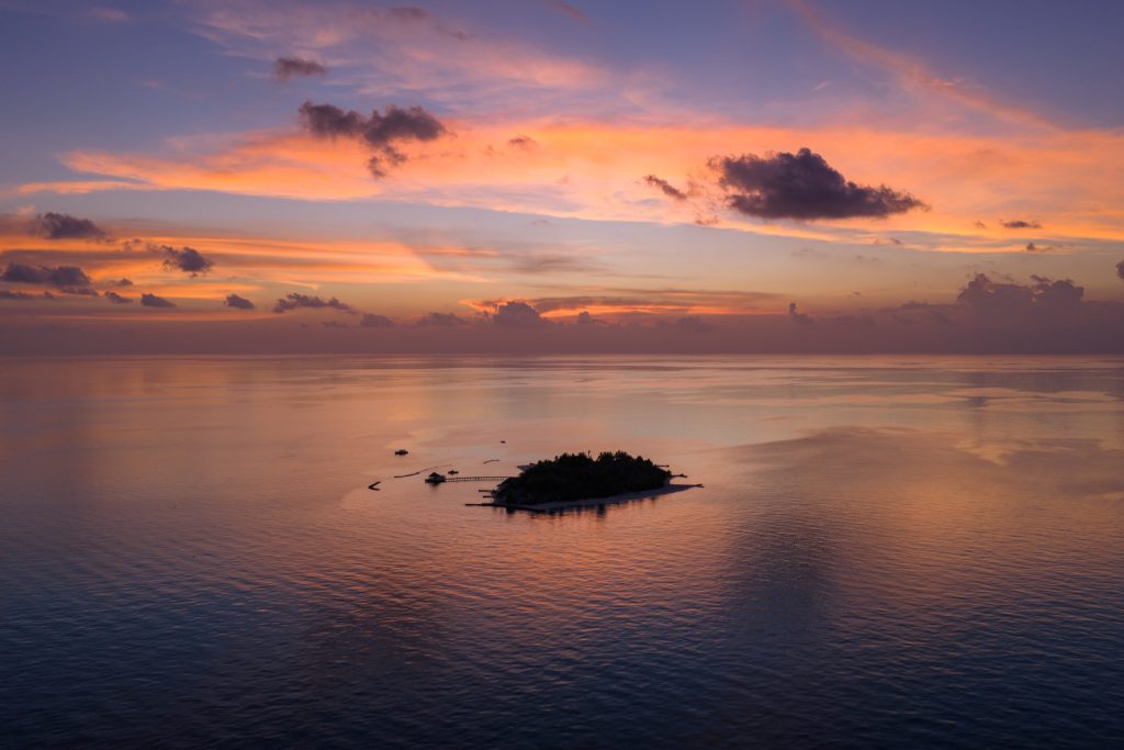 Luftaufnahme einer kleinen Insel mit Gebäuden und Steg umgeben von Wasser bei Sonnenuntergang auf den