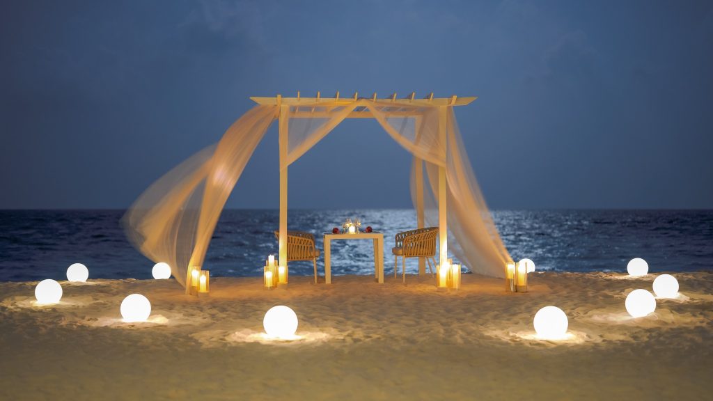 Strand-Pergola mit Tisch, zwei Stühlen, Kerzen und kugelförmigen Lichtern bei Nacht am Eri Maldives