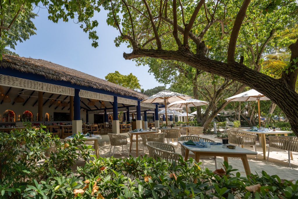 Außenbereich des Eri Maldives Restaurants Soul Kitchen mit Holztischen unter Strohdach und blauen Säulen