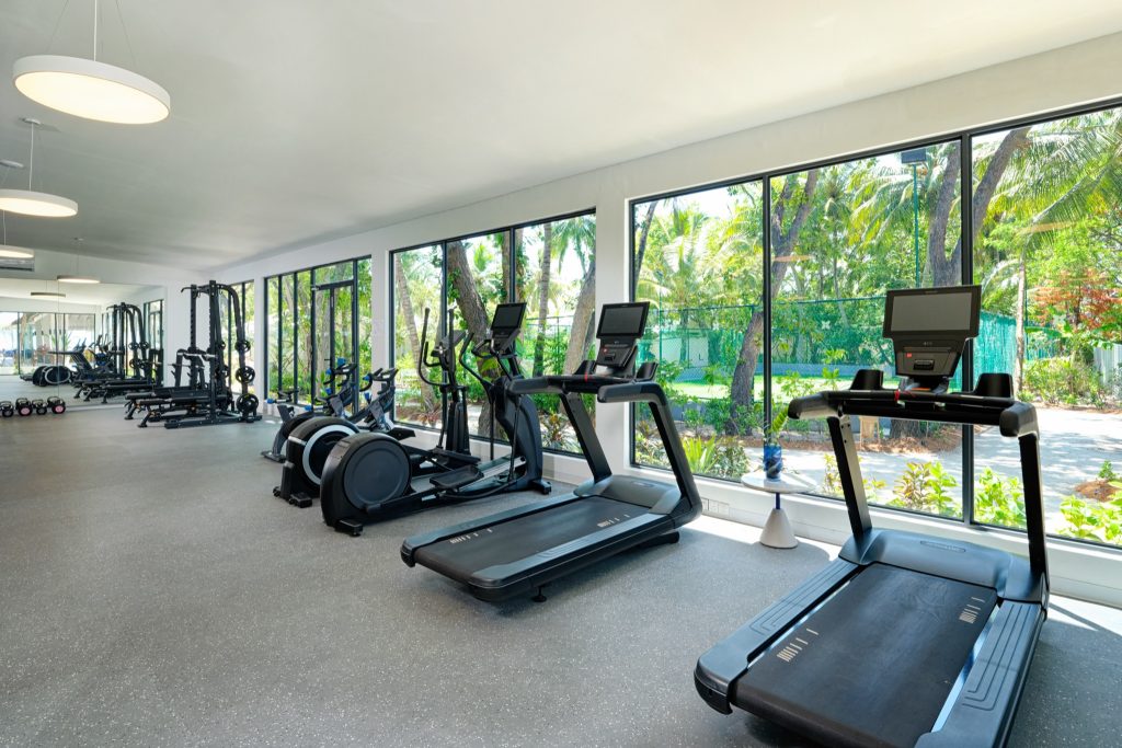 Moderner Fitnessraum im Eri Maldives mit Laufbändern, Rudergeräten und großen Glaswänden mit Blick auf Palmen