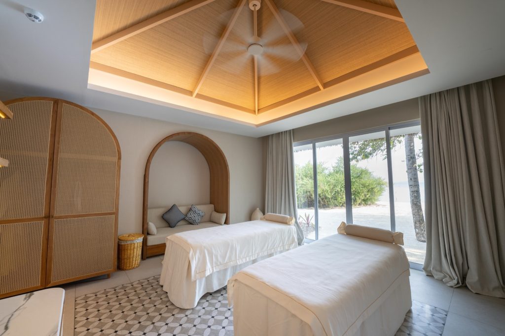 Heller Behandlungsraum im Eri Maldives Wellness Eskape Spa mit zwei weißen Liegen, Holzmöbeln und großen Fenstern