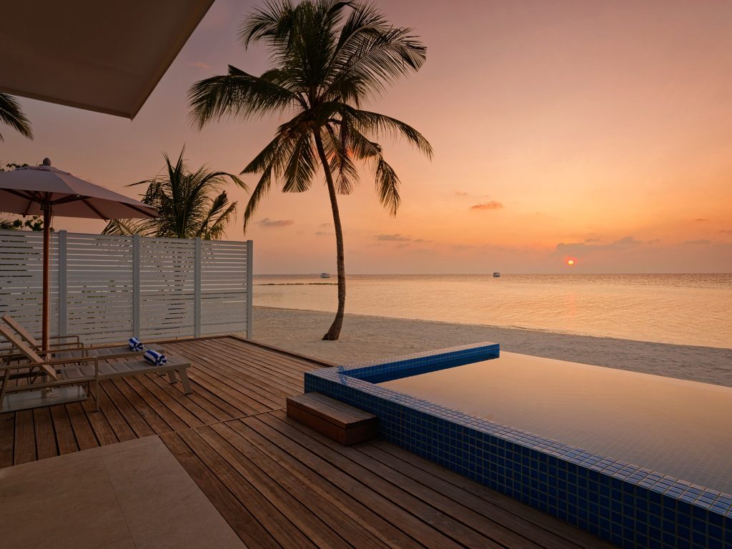 Hotelterrasse mit Infinity-Pool aus blauen Fliesen, Holzdielen, Liegestühlen und Strand auf den