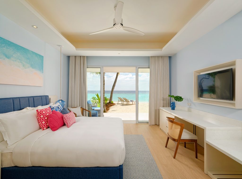 Modernes Beach Villa Zimmer mit großem Bett, blauer Kopfstütze, Holzfußboden und Meerblick durch Glas-Schiebetür