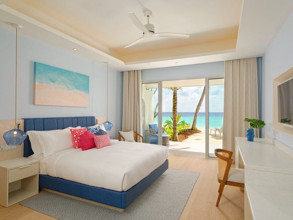Modernes Hotelzimmer der Eri Maldives Beach Villa mit blauem Kopfteil, blauen Glaslampen und Meeresbild an der Wand