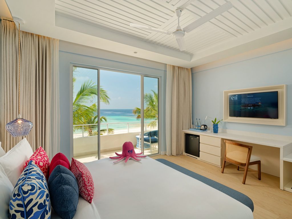 Studio Zimmer im Eri Maldives mit großem Bett, bunten Kissen, Glastür, Palmen und Meerblick