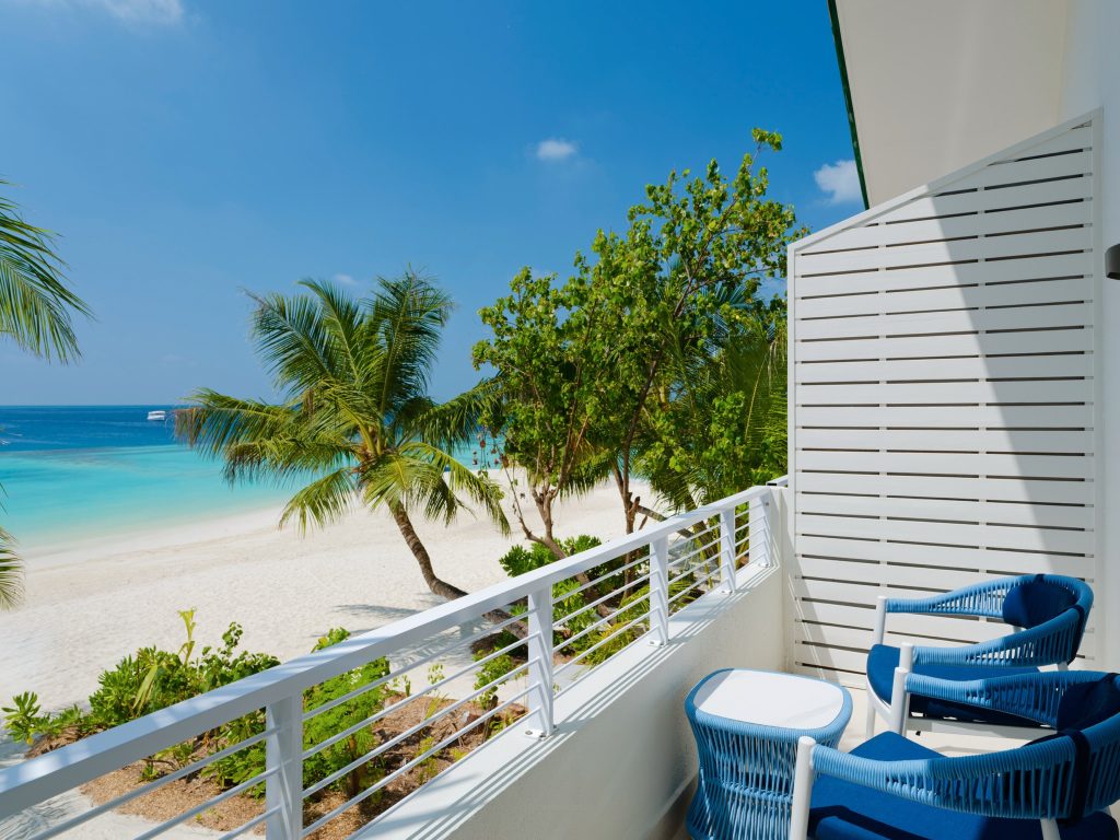 Hotelbalkon mit zwei blauen geflochtenen Sesseln, weißem Metallgeländer und Blick auf Strand und Meer