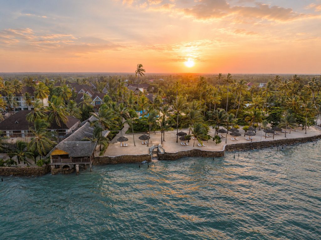 Luftaufnahme des Jaz Amaluna Hotels mit Palmen, Strandliegen und hellen Steingebäuden bei Sonnenuntergang