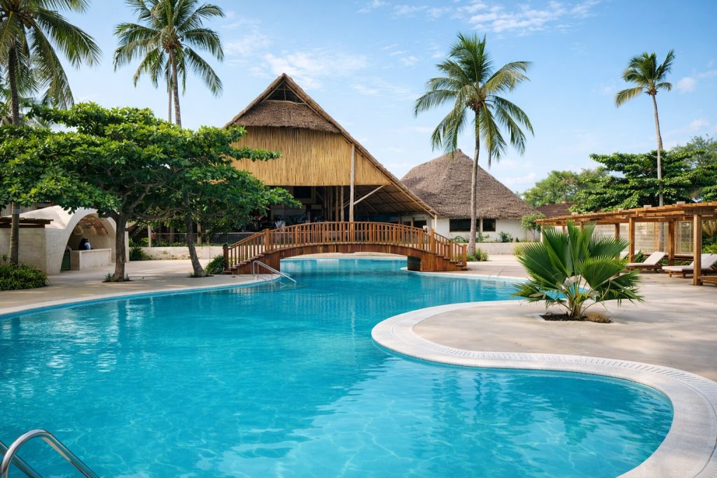 Großer Swimmingpool mit Holzbrücke, Bambusgebäude und tropischen Pflanzen im Hotel Jaz Amaluna auf Sansibar