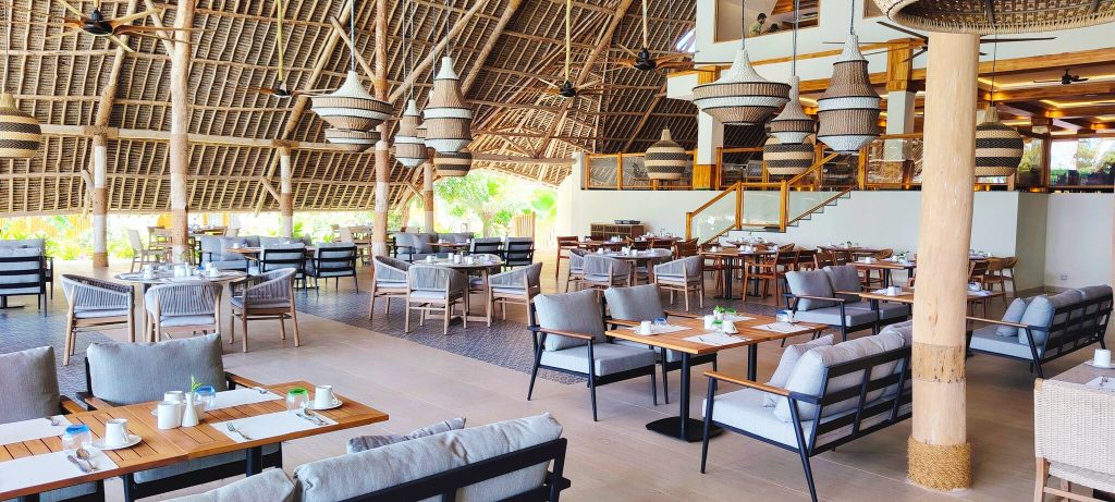 Offenes Restaurant Amani im Jaz Amaluna mit Stroh-Dach, Holz- und Stoffmöbeln in Grau- und Beigetönen und geflochtenen Lampen