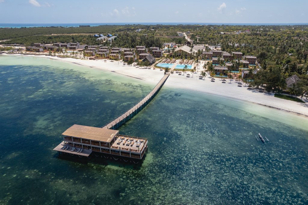 Luftaufnahme des JAZ Elite Aurora Hotels in Sansibar mit Holzsteg über Wasser, Strand, Poolbereich und Palmen