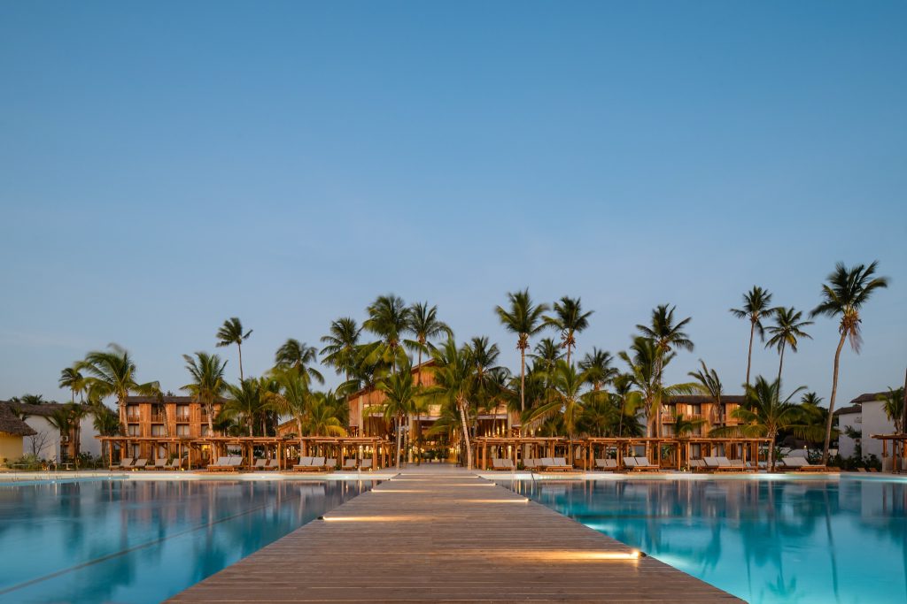Holzsteg über türkisblauem Pool führt zum Hauptgebäude im JAZ Elite Aurora Resort Sansibar