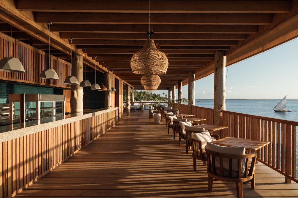 Holzterrasse des Restaurants Samaki mit Meerblick, geflochtenen Lampen und traditionellem Segelboot in Sansibar