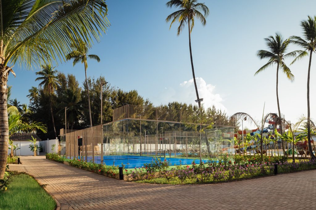 Tennisplatz mit blauem Boden, umgeben von Glaszaun und tropischen Pflanzen im JAZ Elite Aurora Sansibar