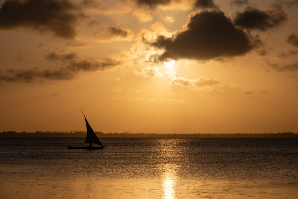 Traditionelles Segelboot segelt bei Sonnenuntergang über ruhiges Wasser am Strand des JAZ Elite Aurora Sansibar