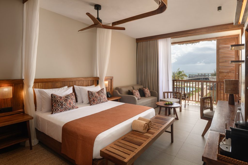 Hotelzimmer im JAZ Elite Aurora mit großem Bett, Holzmöbeln, Balkon und Meerblick auf Sansibar