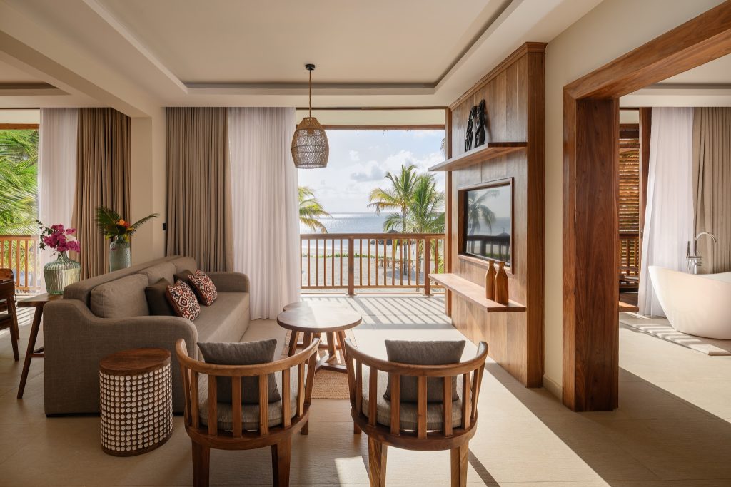 Modernes Hotelzimmer Royal Suite mit Holzsesseln, Holztisch, grauem Sofa und Meerblick in JAZ Elite Aurora Sansibar