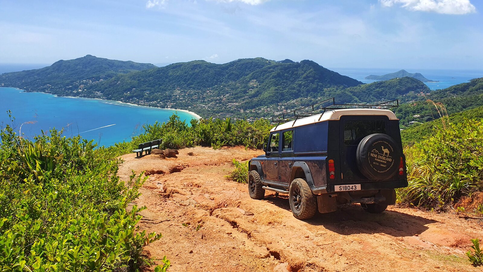 Geländewagen auf staubigem Pfad in hügeliger Landschaft mit Blick auf Küste und Lagune auf Mahé, Seychellen