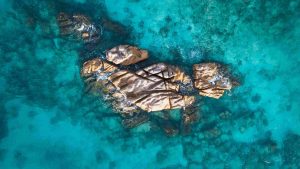 Gruppe von Granitfelsen im türkisblauen Wasser des Indischen Ozeans bei Praslin, aufgenommen aus der Luft ohne Boote.