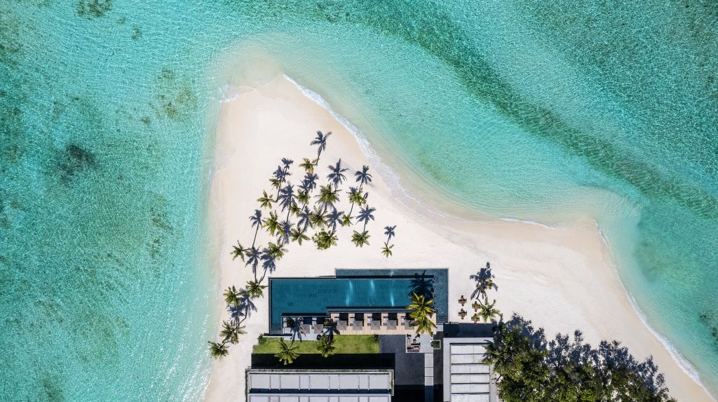 Luftaufnahme des Alila Kothaifaru Maldives mit langgestrecktem Pool, Liegestühlen, Palmen und türkisfarbenem Meer