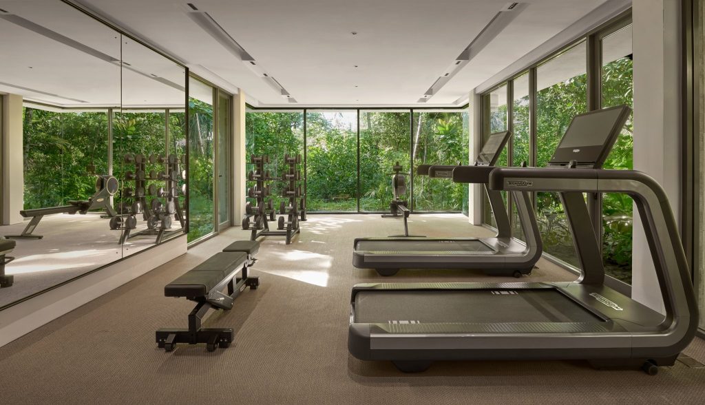 Moderner Fitnessraum im Alila Kothaifaru Maldives mit Laufbändern, Hanteln und Glaswänden mit Blick auf grüne Pflanzen