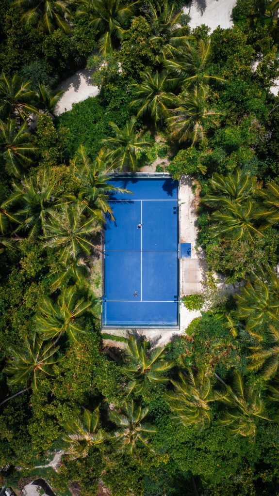 Tennisplatz mit blauem Hartplatz und weißen Linien, umgeben von grünen Palmen auf den Malediven aus der Vogelperspektive