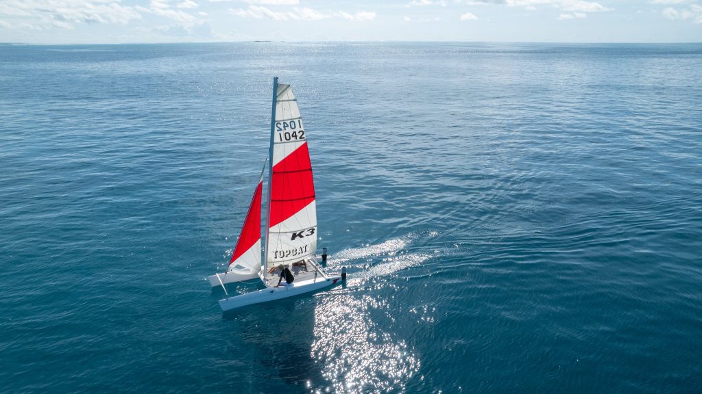 Segelboot mit weißen und roten Segeln auf tiefblauem Meer bei leicht bewölktem Himmel auf den