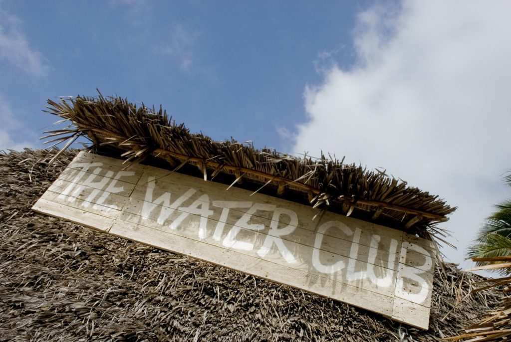 Traditionelles Strohdach mit Holzschild THE WATER CLUB unter blauem Himmel im Breezes Beach Club And Spa Sansibar