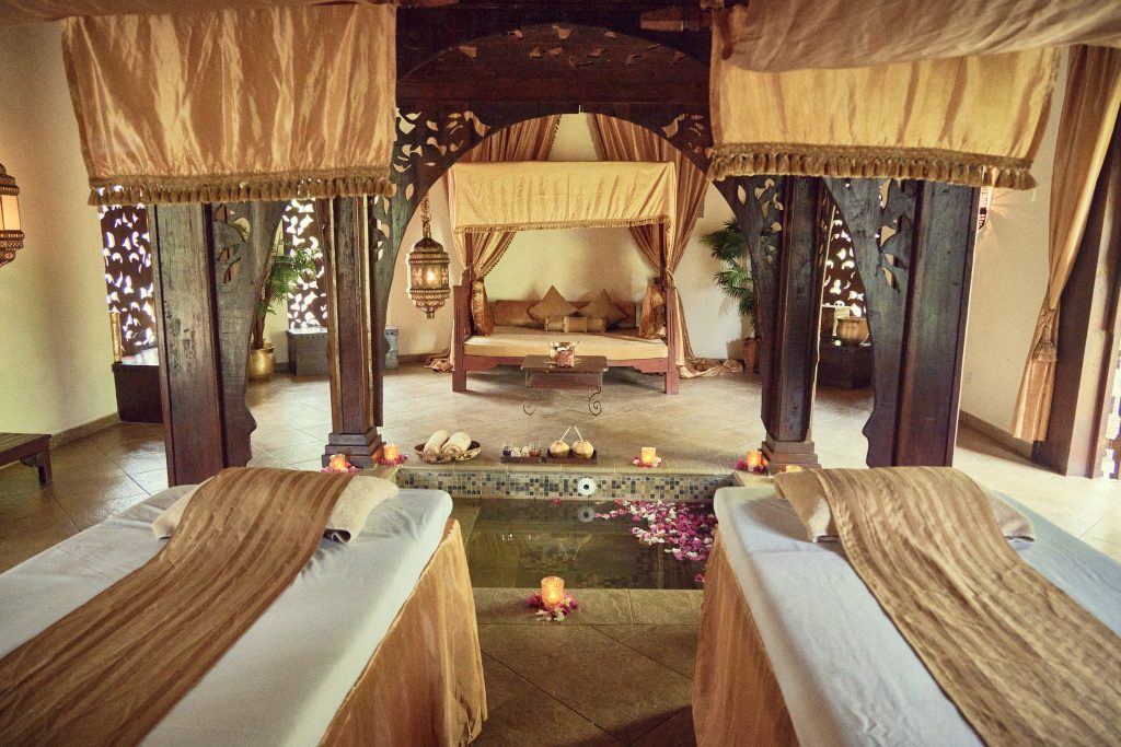Spa-Bereich mit zwei Massagebänken, Wasserbecken mit Blütenblättern und brennenden Kerzen im Frangipani Spa