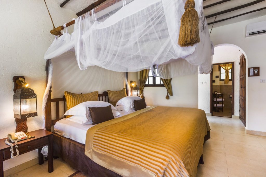Deluxe Room im Breezes Beach Club And Spa mit großem Bett, weißem Moskitonetz, dunklen Holzmöbeln und offenem Badezimmer