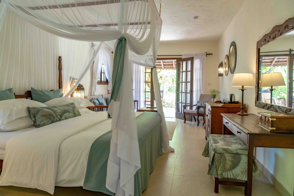 Gemütliches Zimmer im Breezes Beach Club And Spa mit Himmelbett, Holzmöbeln und Blick auf den Garten in Sansibar