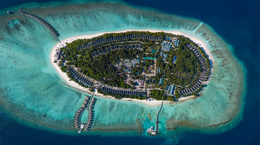 Insel mit Gebäuden und Wasserbungalows über türkisfarbenem Meer umgeben von grüner Vegetation