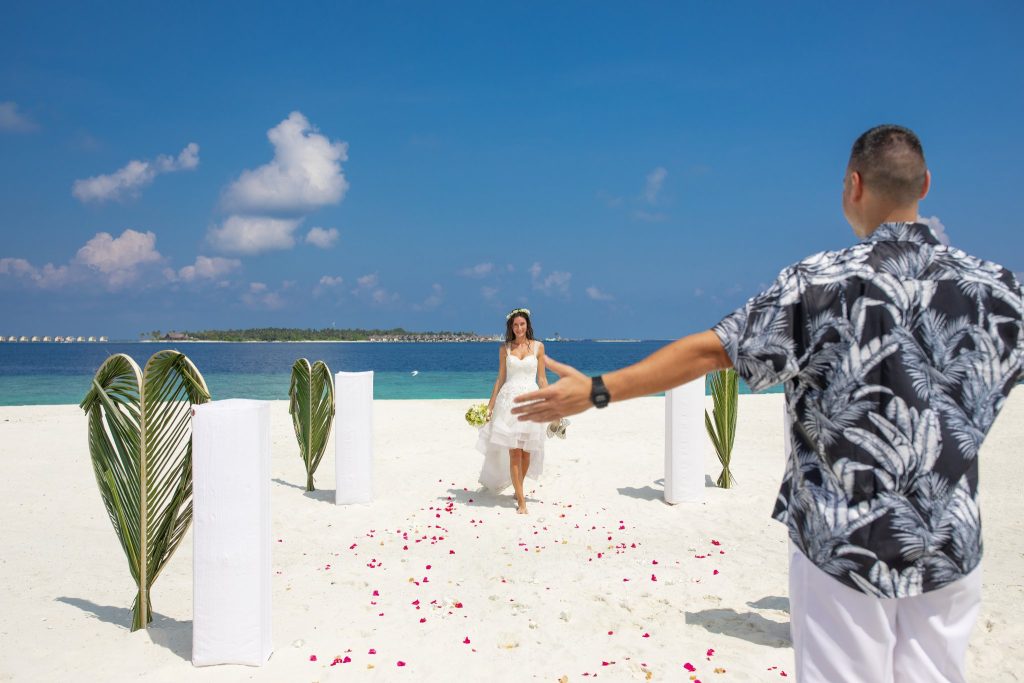 Strandhochzeit am weißen Sand mit Palmenblättern und weißen Stoffsäulen unter blauem Himmel auf Furaveri Maldives