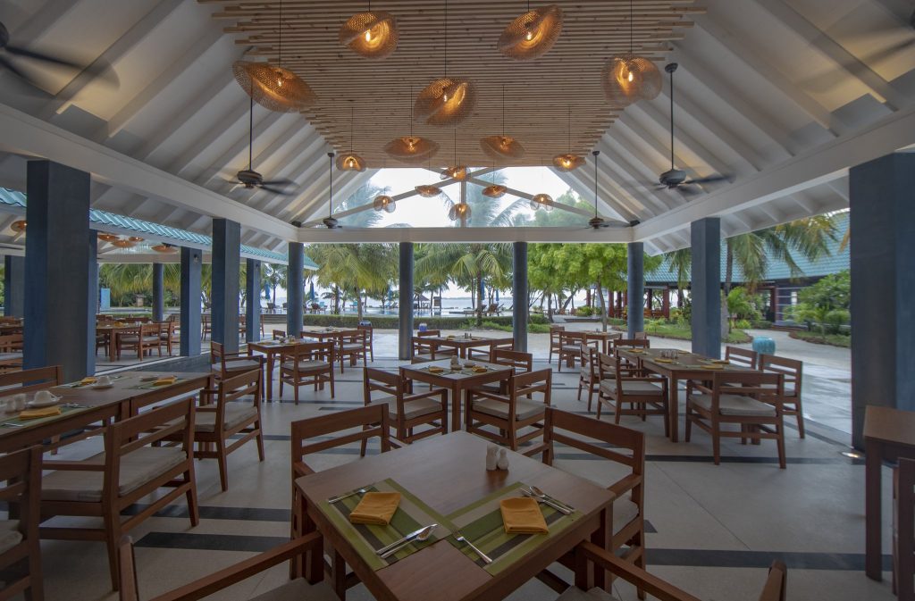 Offenes Restaurant Jaafaiy im Furaveri Maldives mit weißen Holzdach, Holztischen, Steinboden und Blick auf Palmen