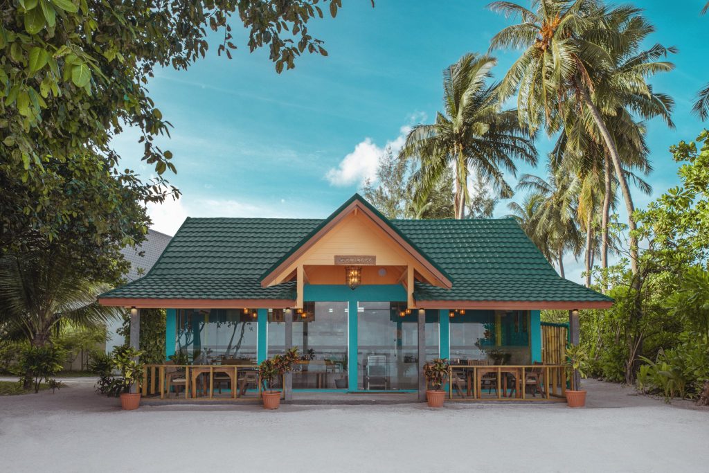 Kleines Restaurant Ocean Spice mit grünem Dach, Holz-Glas-Fassade und Holztischen, umgeben von Palmen auf den