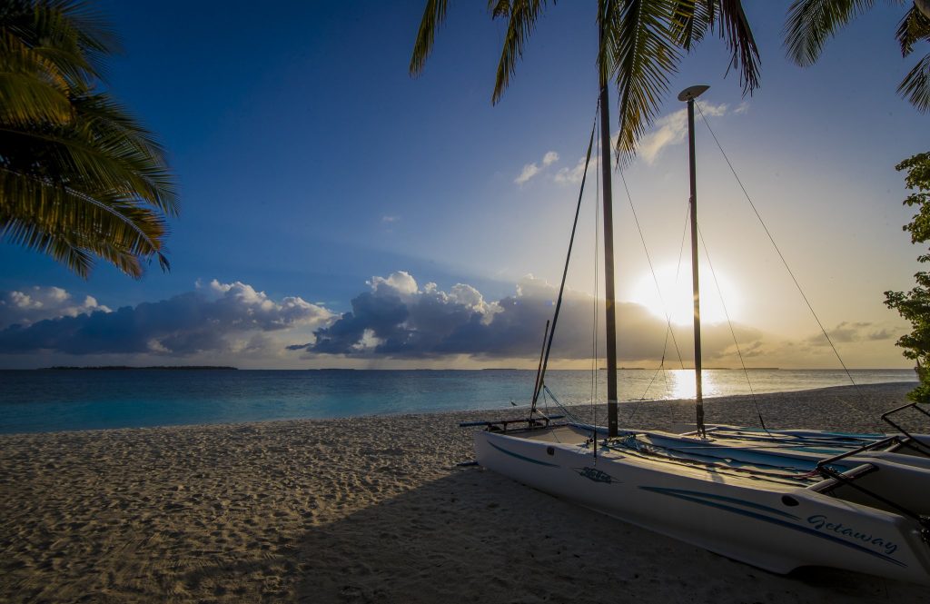 Katamaran aus Glasfaser und Metall auf Sandstrand bei Sonnenuntergang mit Palmen und blauem Himmel auf den