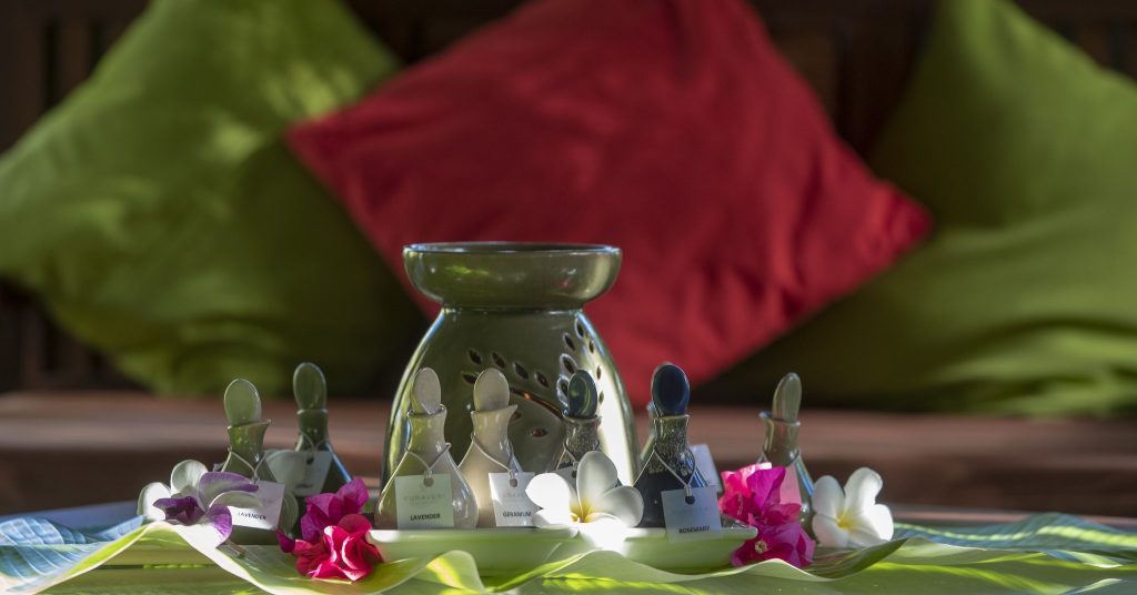 Mehrere kleine Glasflaschen mit Aromabezeichnungen auf weißem Tablett, dekoriert mit exotischen Blumen und grünen Blättern