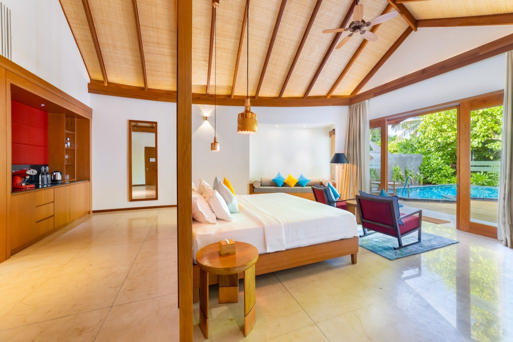 Modernes Hotelzimmer mit Holzdecke, Sofa, Bett, großem Fenster und Blick auf Terrasse mit Pool und Grün