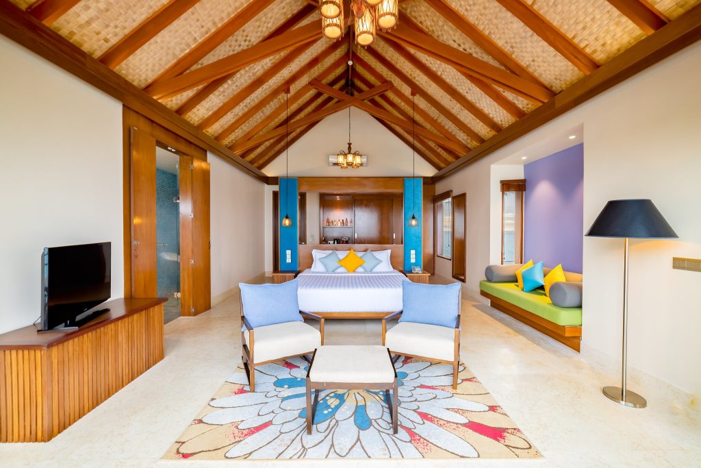 Geräumiges Zimmer Ocean Villa Horizon mit schräger Holzdecke, großem Bett, blauen Wänden und Jacuzzi auf den