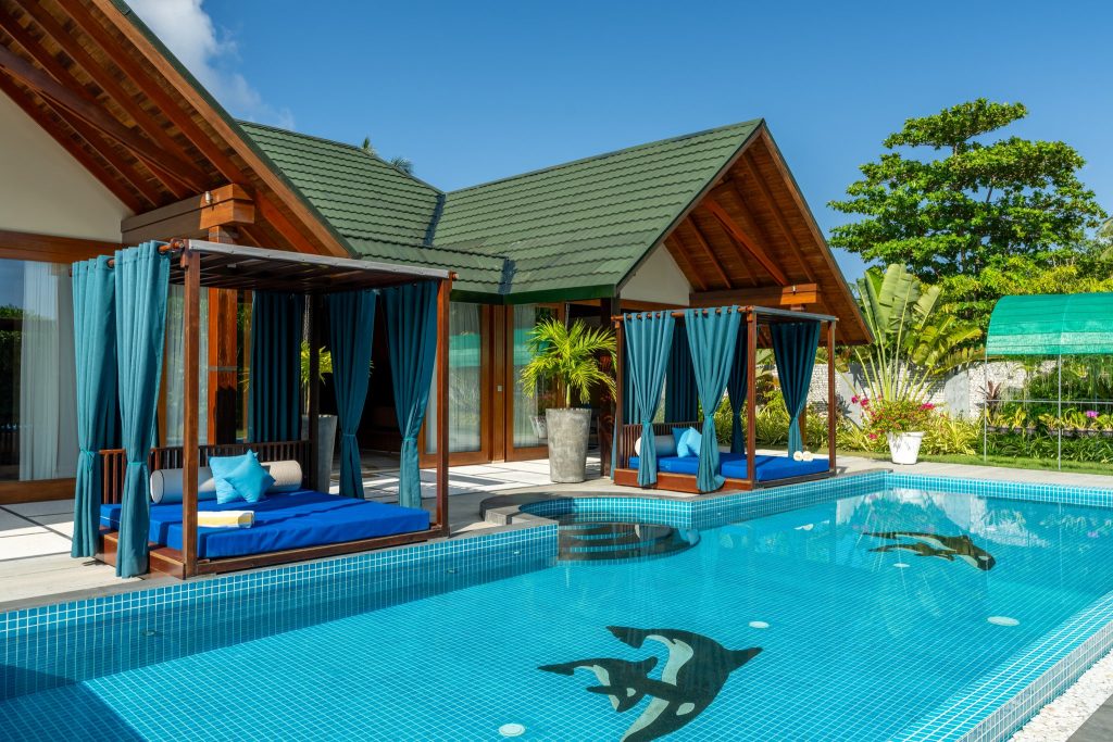 Pool mit türkisblauem Wasser und schwarz-weißen Delphinmotiven, Tagesbetten unter petrolfarbenen Vorhängen