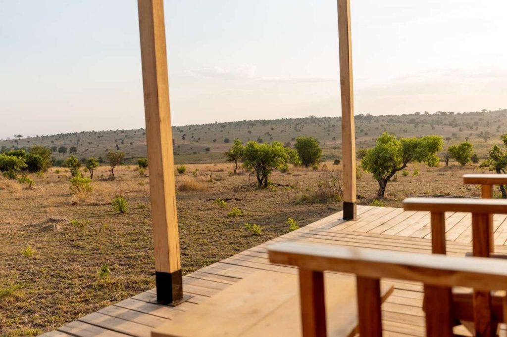Terrasse aus hellem Holz mit Holzmöbeln und Blick auf trockene Savannenlandschaft in Tansania