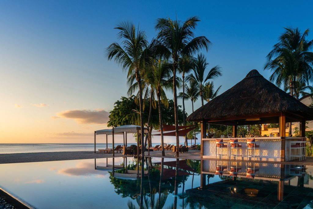 Infinity-Pool vor der Bar Hibiscus mit Strohdach, Palmen und Strand im Hintergrund bei Sonnenuntergang